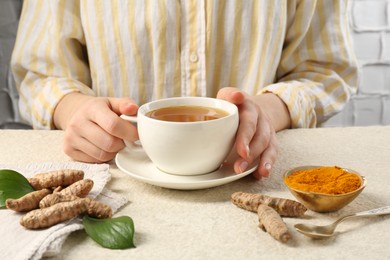 Photo of Woman drinking turmeric tea at white textured table, closeup