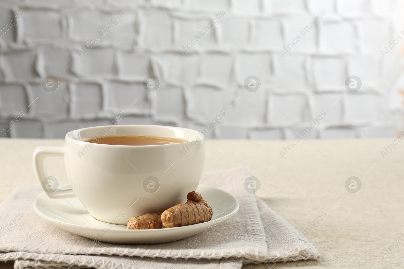 Photo of Aromatic turmeric tea and rhizomes on white textured table. Space for text