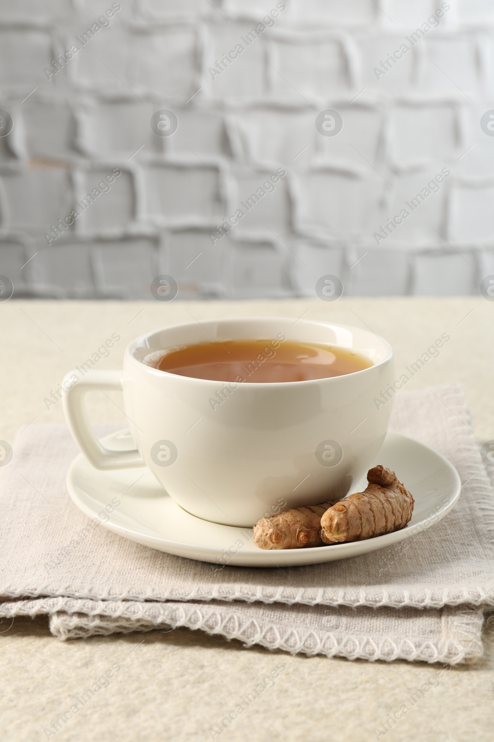 Photo of Aromatic turmeric tea and rhizomes on white textured table. Space for text