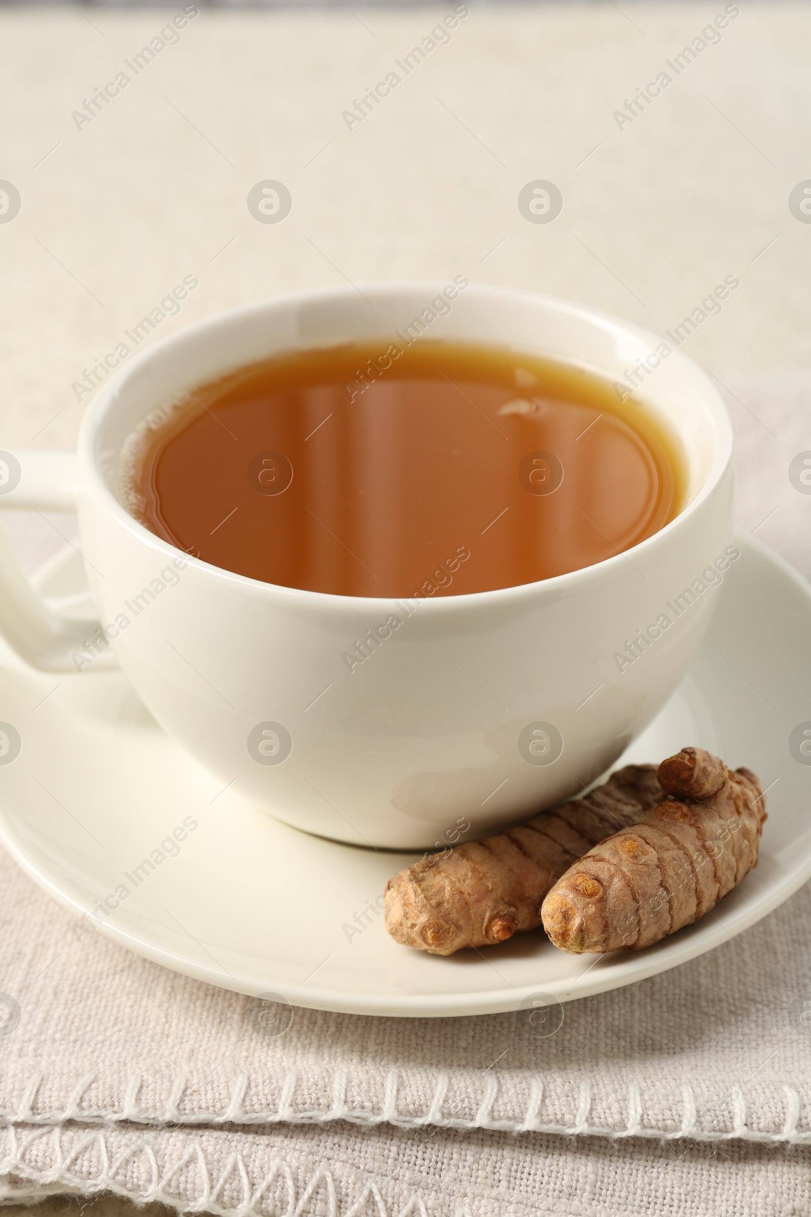 Photo of Aromatic turmeric tea and rhizomes on white textured table, closeup