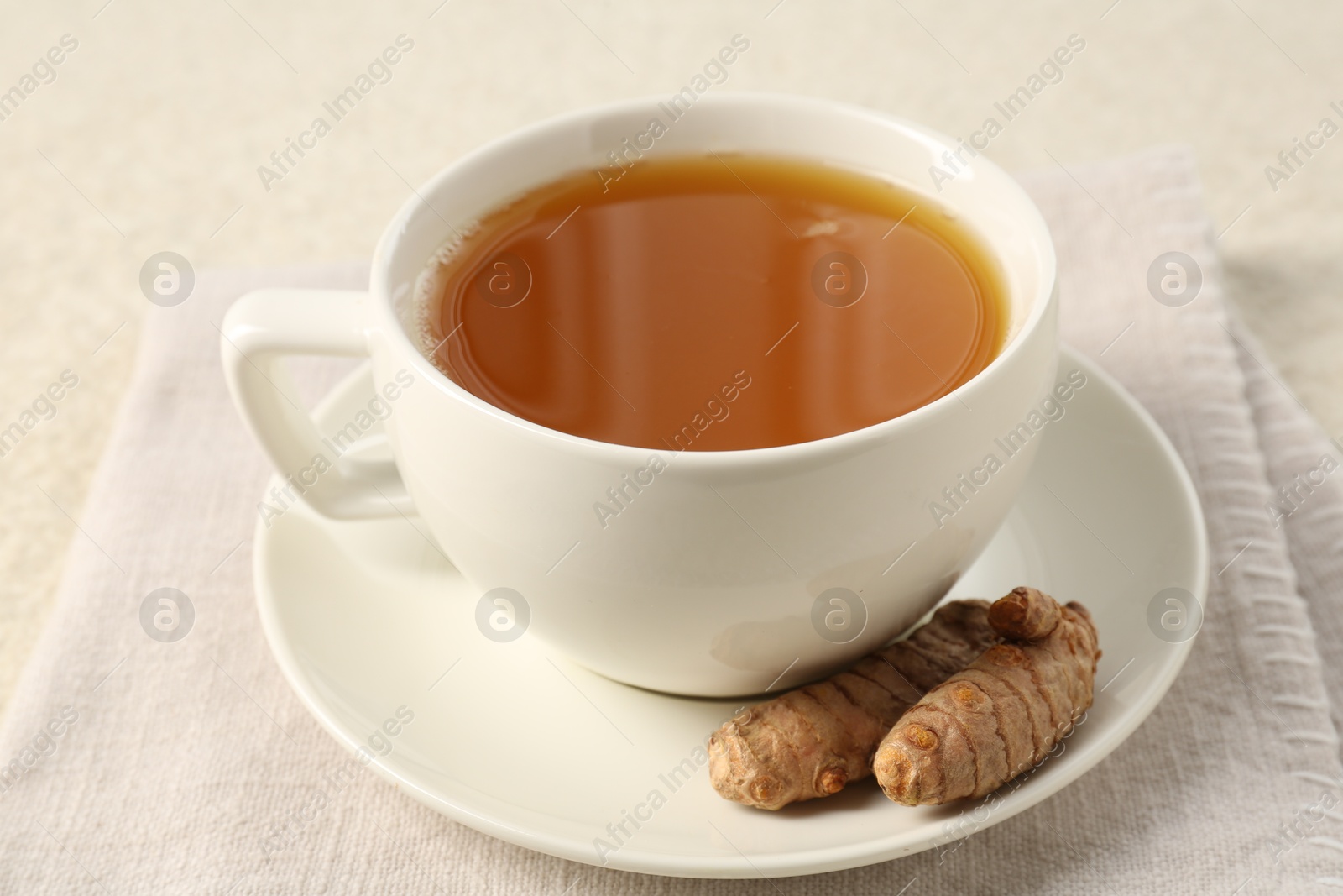 Photo of Aromatic turmeric tea and rhizomes on white textured table, closeup