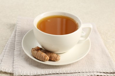 Photo of Aromatic turmeric tea and rhizomes on white textured table, closeup