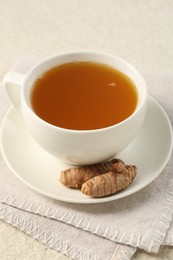 Photo of Aromatic turmeric tea and rhizomes on white textured table, closeup