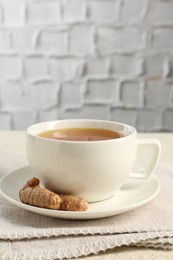 Photo of Aromatic turmeric tea and rhizomes on white textured table. Space for text