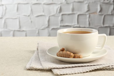 Photo of Aromatic turmeric tea and rhizomes on white textured table. Space for text