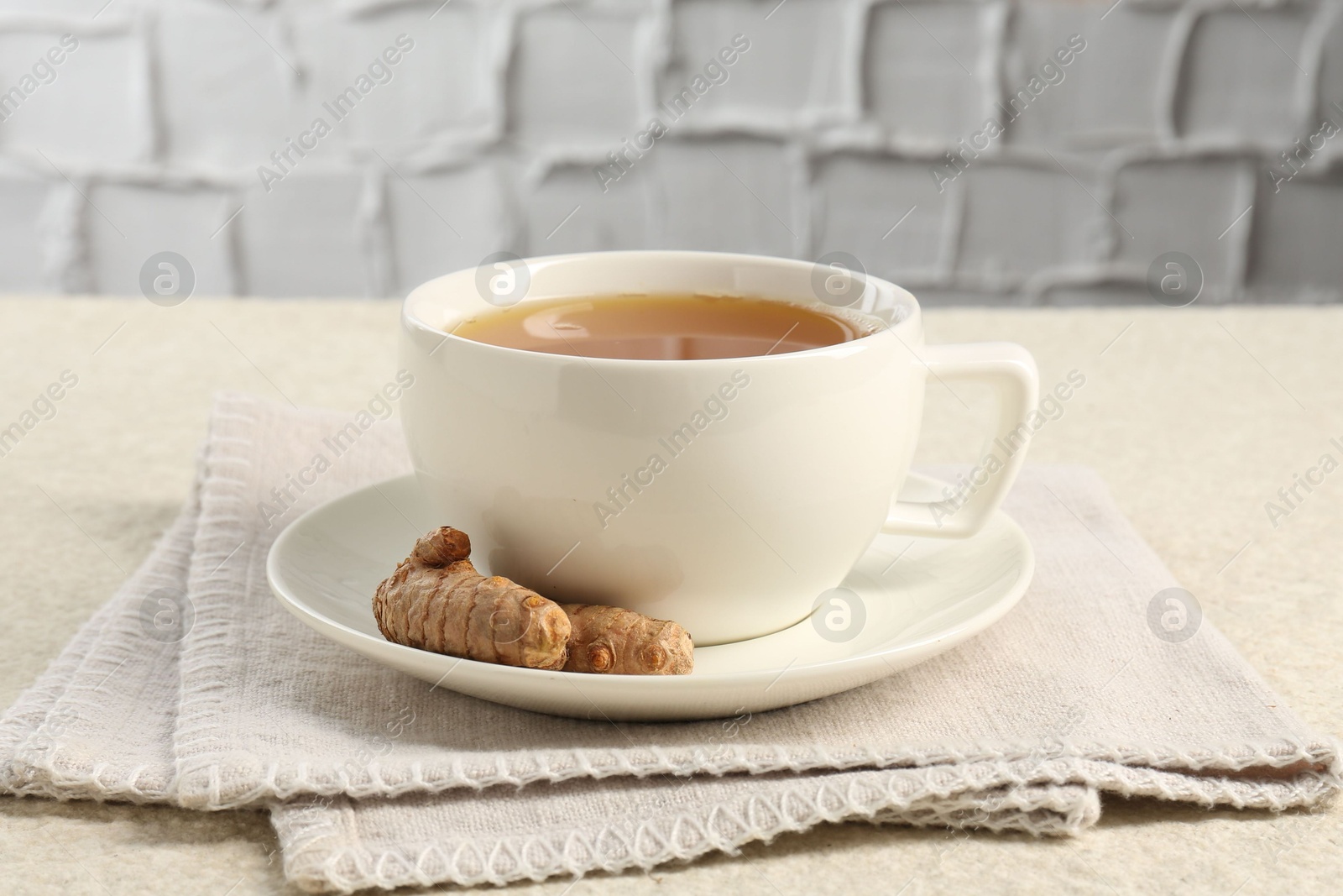 Photo of Aromatic turmeric tea and rhizomes on white textured table, closeup