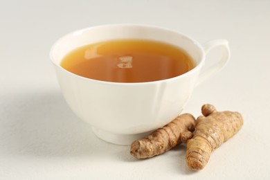 Photo of Aromatic turmeric tea and rhizomes on white table, closeup