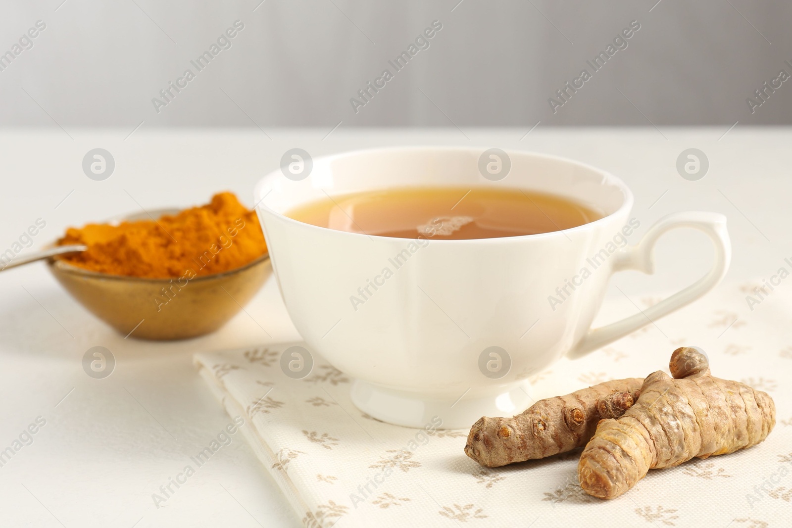 Photo of Aromatic turmeric tea, powder and rhizomes on white table, closeup