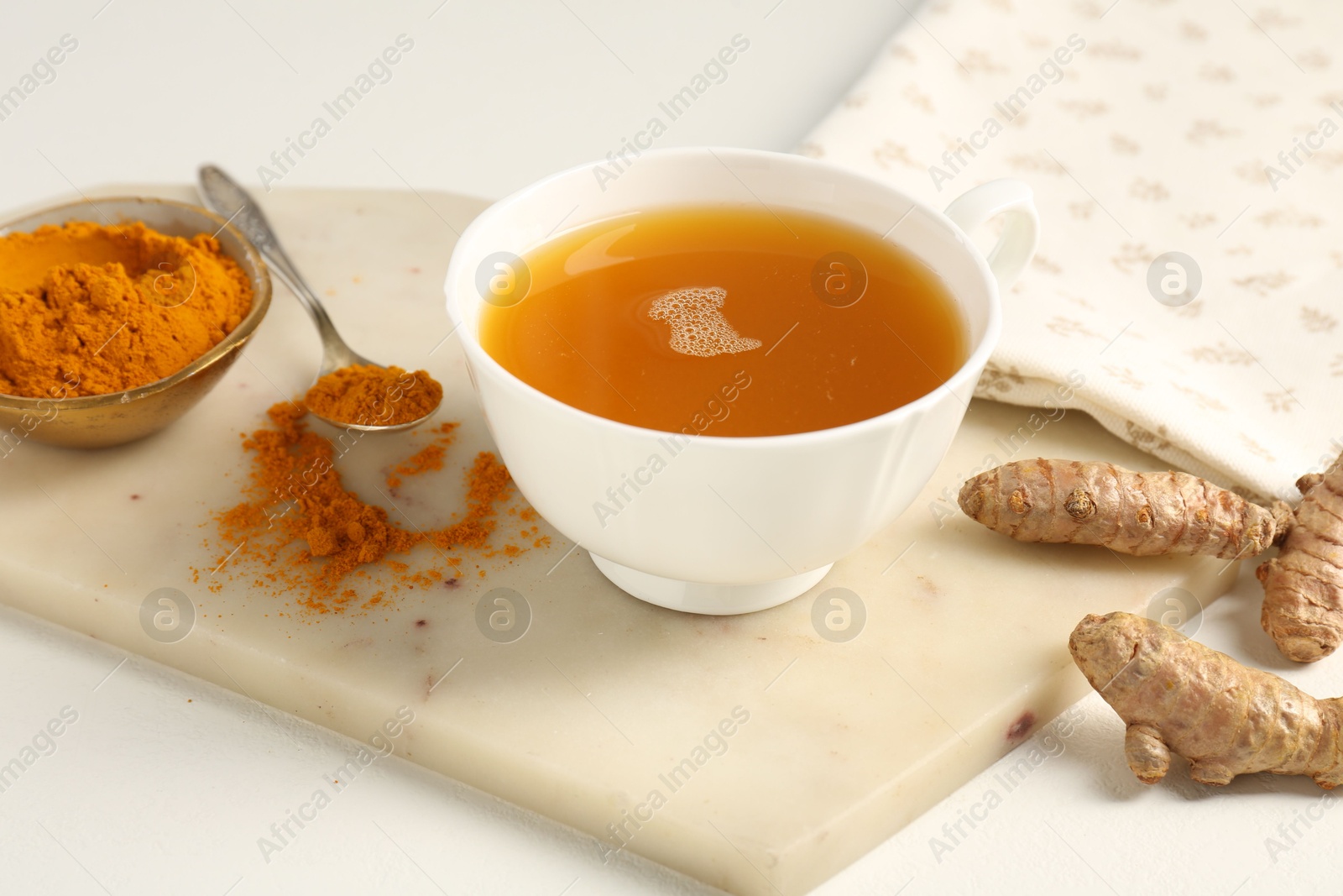 Photo of Aromatic turmeric tea, powder and rhizomes on white table, closeup