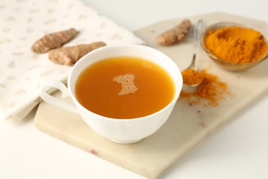 Photo of Aromatic turmeric tea, powder and rhizomes on white table, closeup