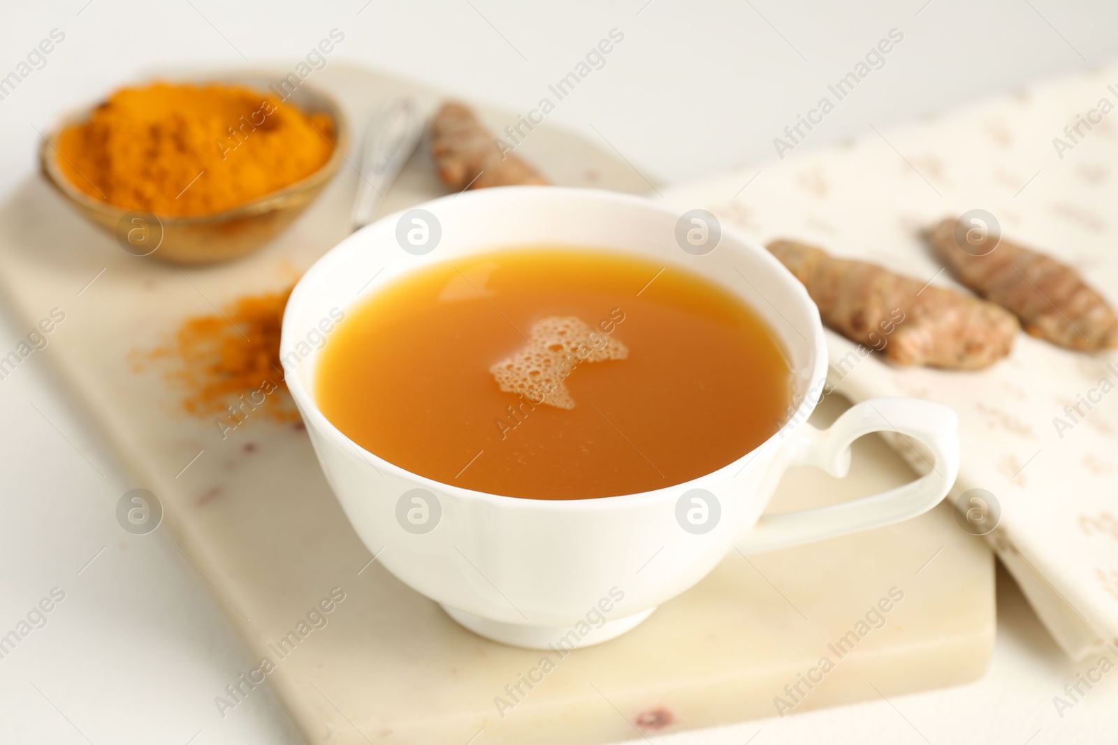 Photo of Aromatic turmeric tea, powder and rhizomes on white table, closeup