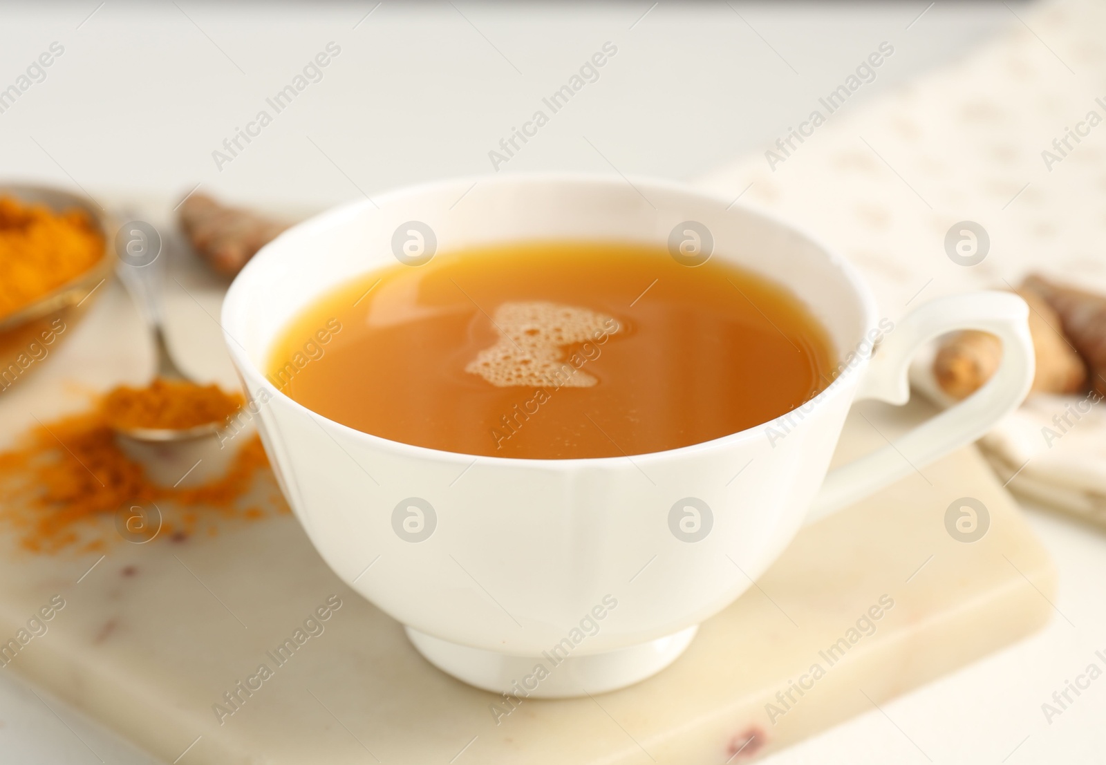 Photo of Aromatic turmeric tea, powder and rhizomes on white table, closeup