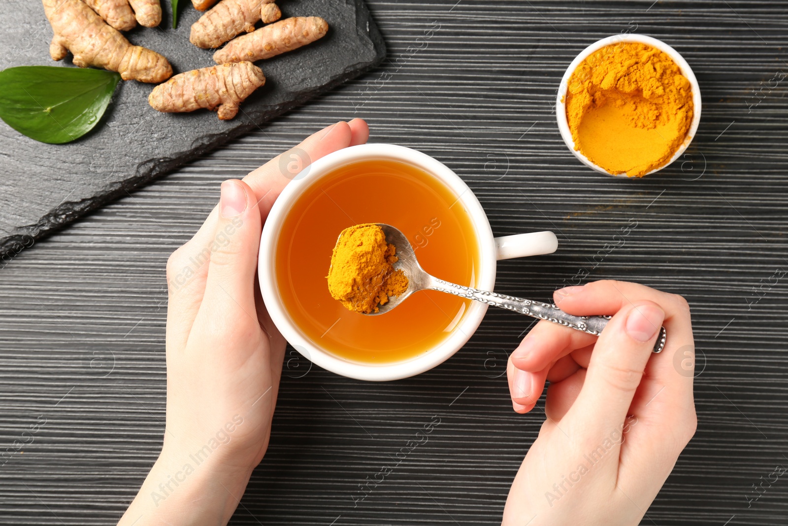 Photo of Woman making turmeric tea at black table, top view