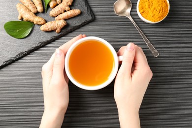 Photo of Woman drinking turmeric tea at black table, top view