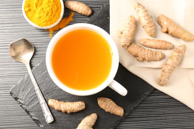 Photo of Aromatic turmeric tea, powder and rhizomes on black table, flat lay