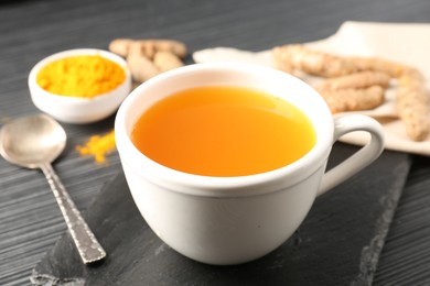 Photo of Aromatic turmeric tea, powder and rhizomes on black table, closeup