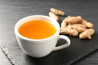 Photo of Aromatic turmeric tea and rhizomes on black table, closeup