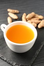 Photo of Aromatic turmeric tea and rhizomes on black table, closeup