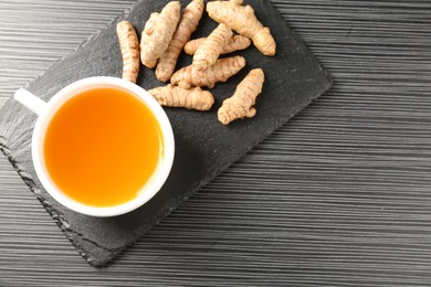 Photo of Aromatic turmeric tea and rhizomes on black table, top view. Space for text