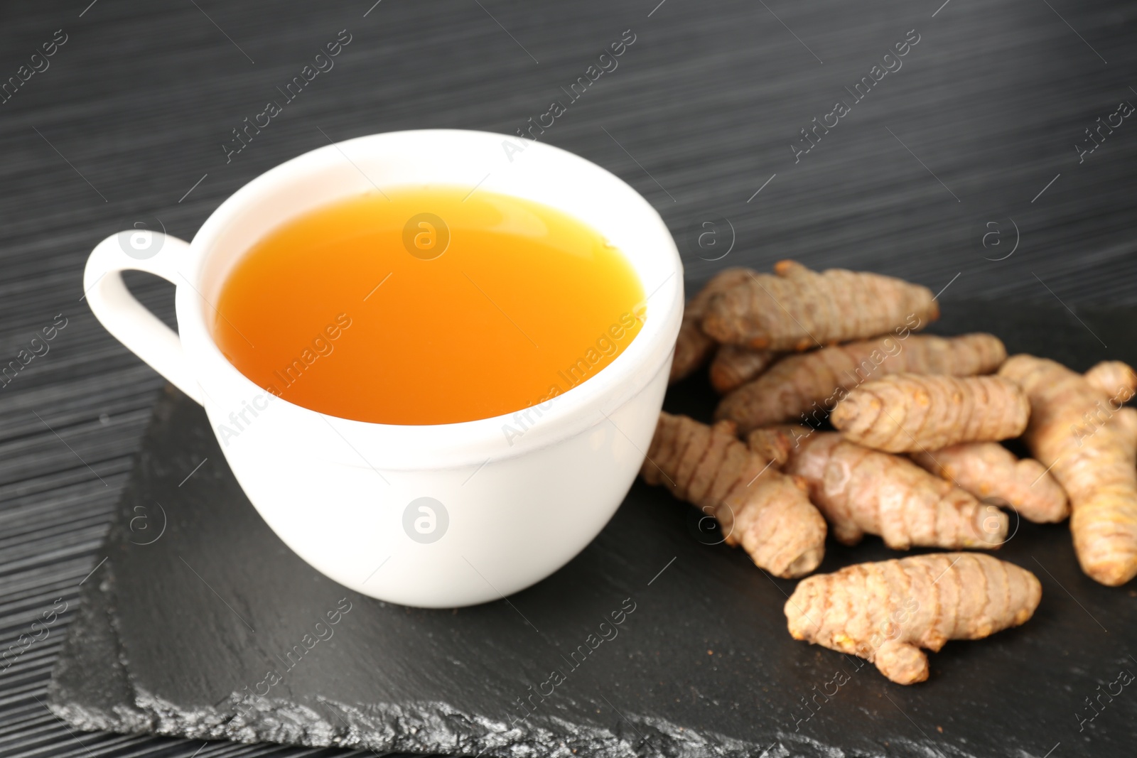 Photo of Aromatic turmeric tea and rhizomes on black table, closeup