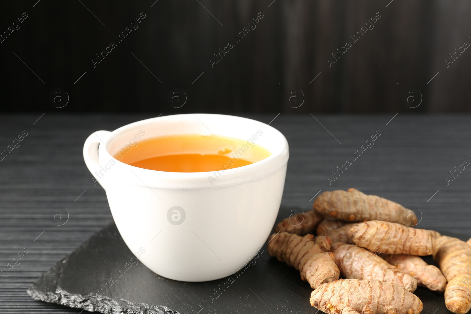 Photo of Aromatic turmeric tea and rhizomes on black table, closeup