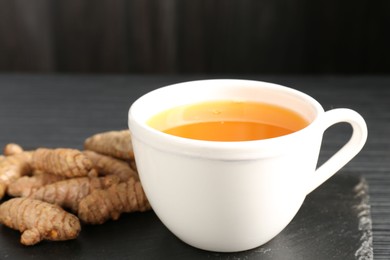 Photo of Aromatic turmeric tea and rhizomes on black table, closeup