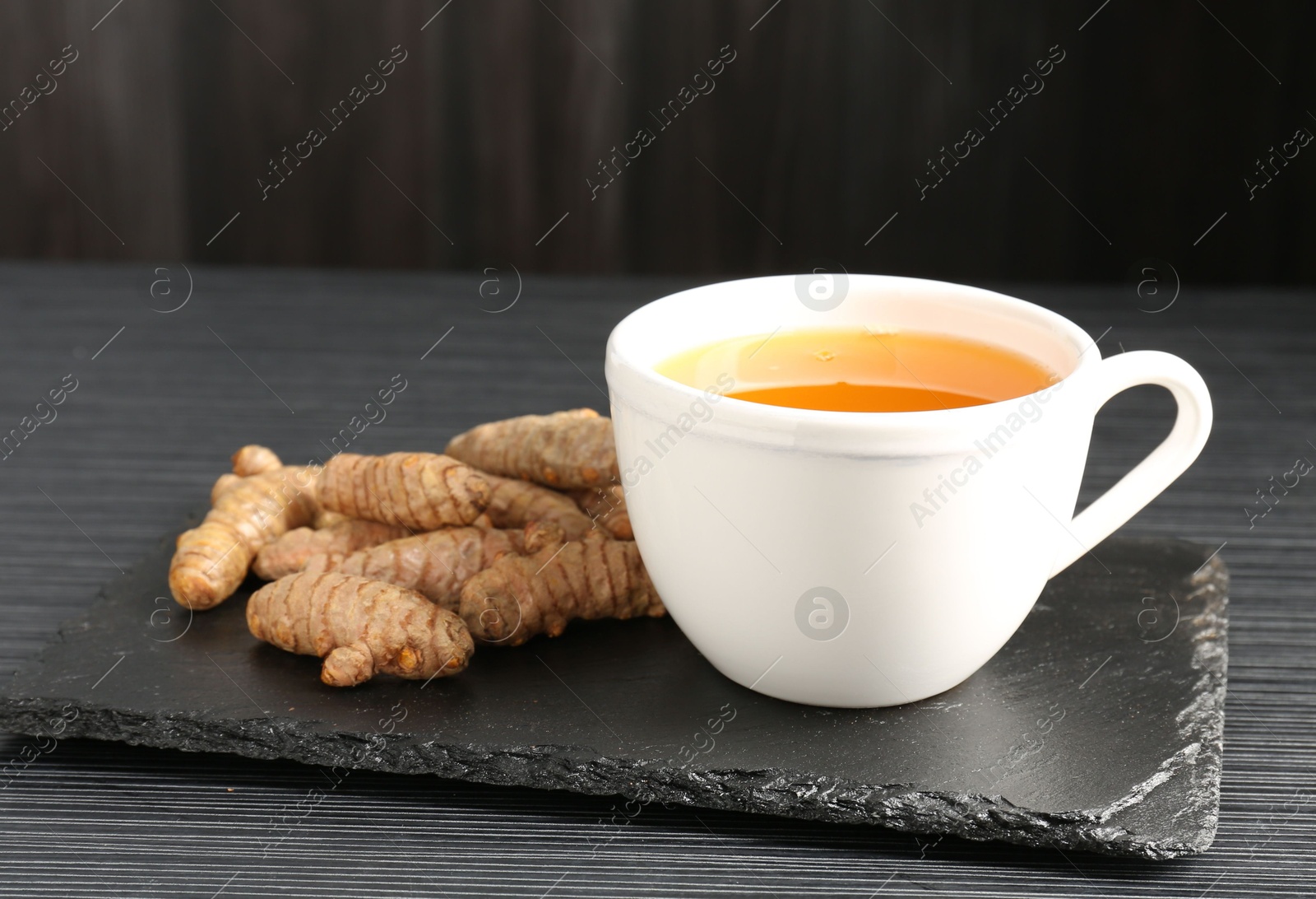 Photo of Aromatic turmeric tea and rhizomes on black table, closeup