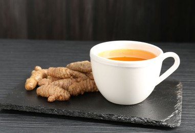 Photo of Aromatic turmeric tea and rhizomes on black table, closeup