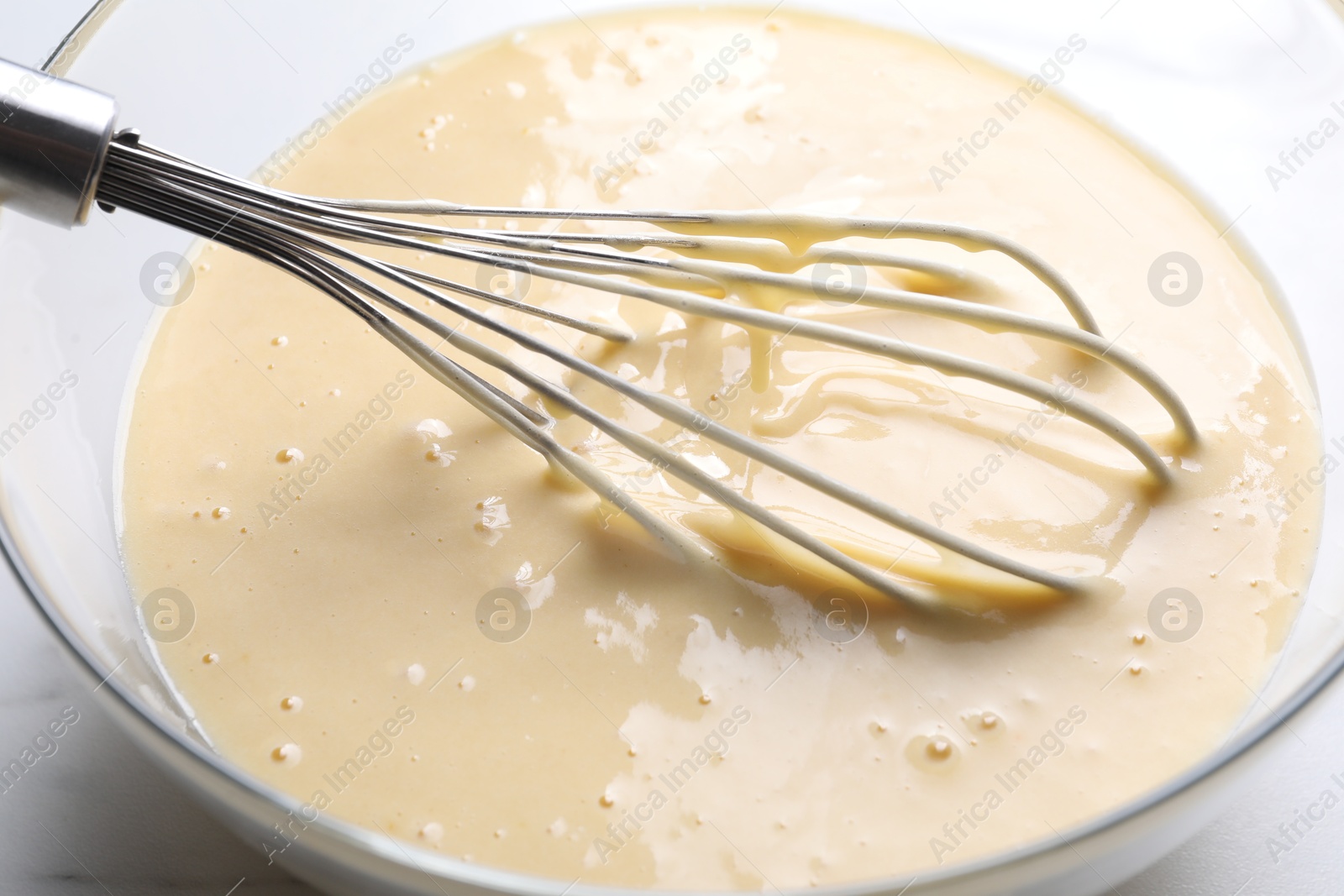 Photo of Whisk and bowl of dough on white table, closeup