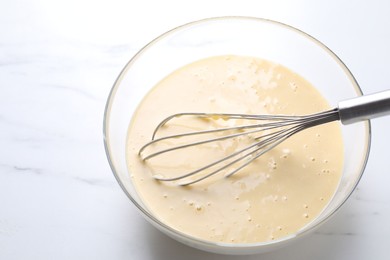 Photo of Whisk and bowl of dough on white marble table, above view. Space for text