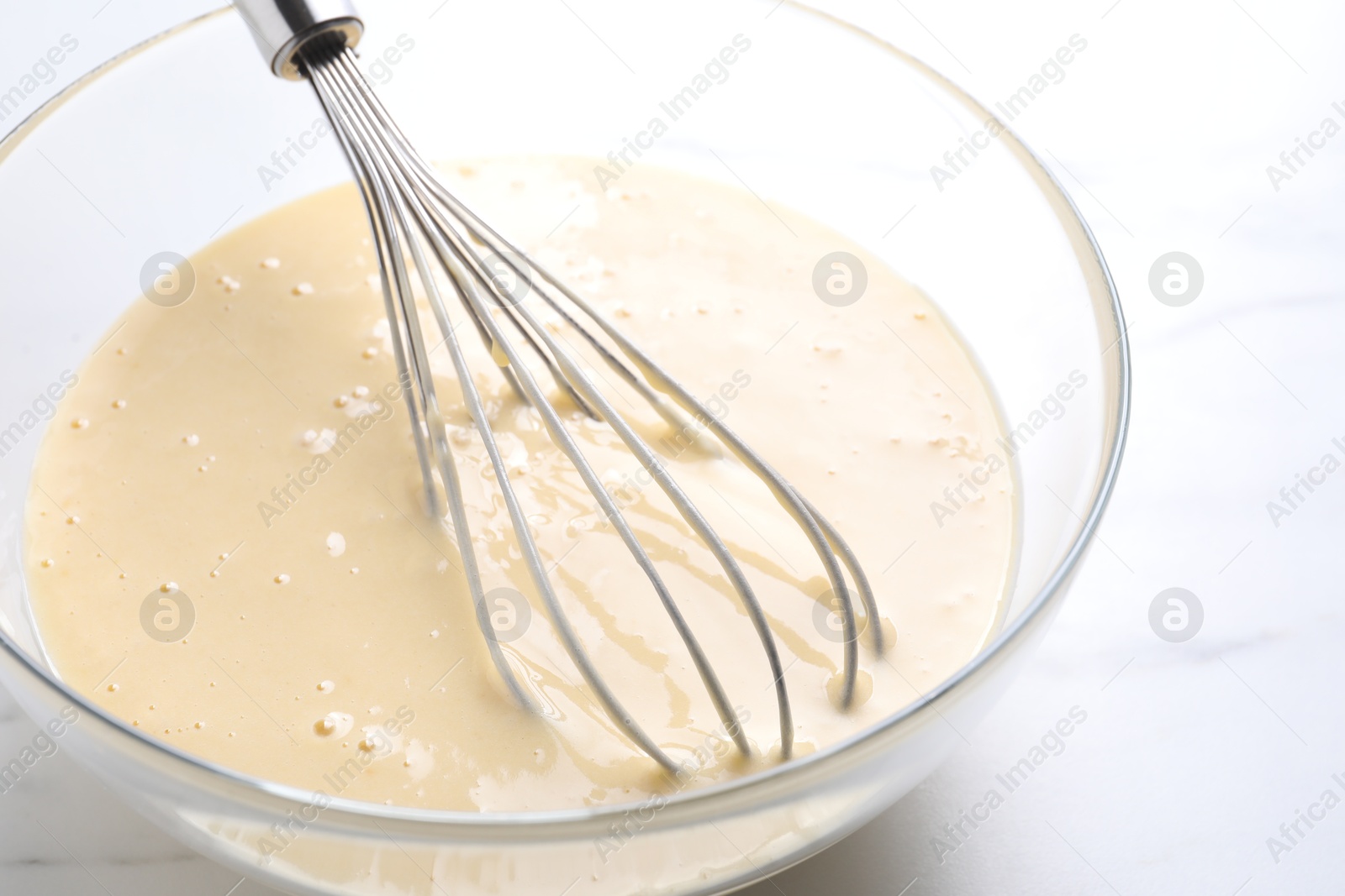 Photo of Whisk and bowl of dough on white marble table, closeup