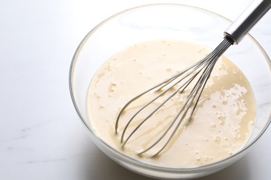 Photo of Whisk and bowl of dough on white marble table, closeup. Space for text