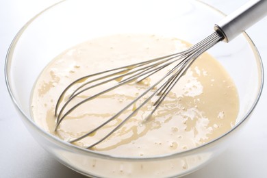 Photo of Whisk and bowl of dough on white table, closeup