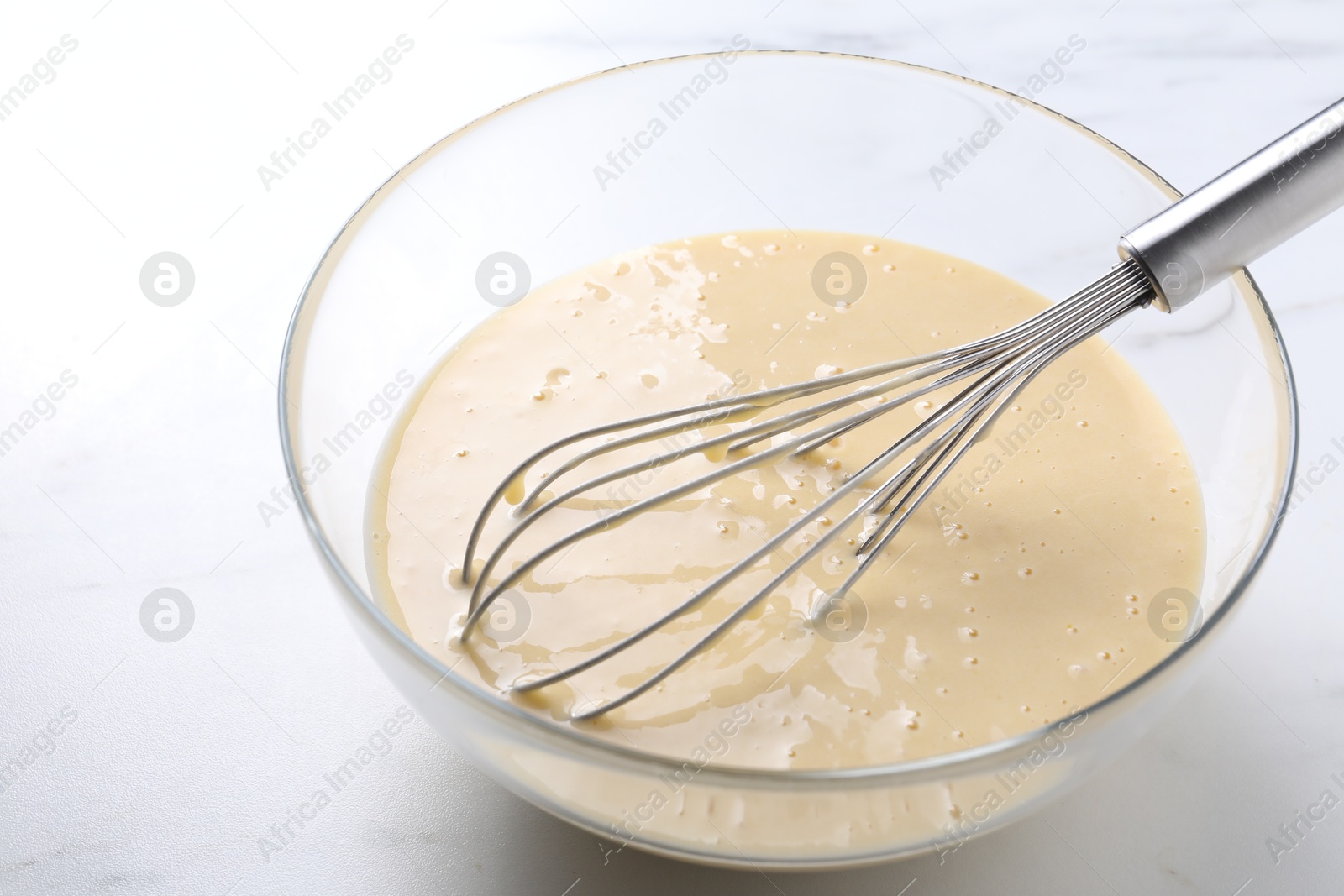 Photo of Whisk and bowl of dough on white table, closeup