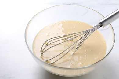 Photo of Whisk and bowl of dough on white table, closeup