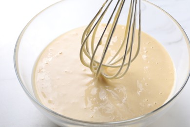 Photo of Whisk and bowl of dough on white table, closeup