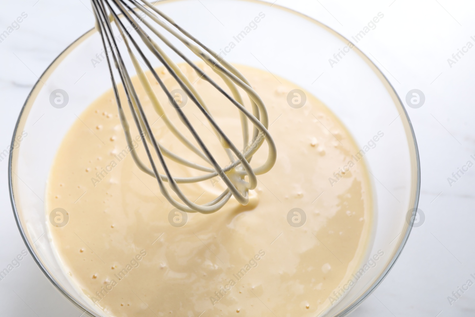 Photo of Whisk and bowl of dough on white table, above view