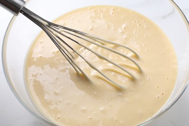 Photo of Whisk and bowl of dough on table, closeup