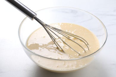 Photo of Whisk and bowl of dough on white marble table, closeup