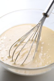 Photo of Whisk and bowl of dough on table, closeup