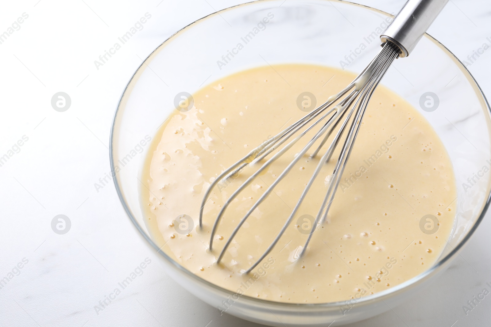 Photo of Whisk and bowl of dough on white marble table, closeup. Space for text