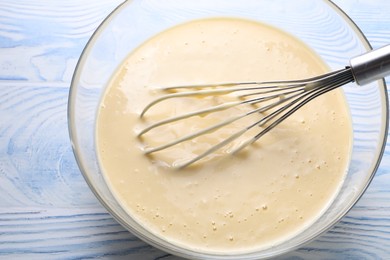 Photo of Whisk and bowl of dough on light blue wooden table, above view