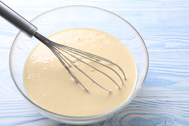 Photo of Whisk and bowl of dough on light blue wooden table, closeup