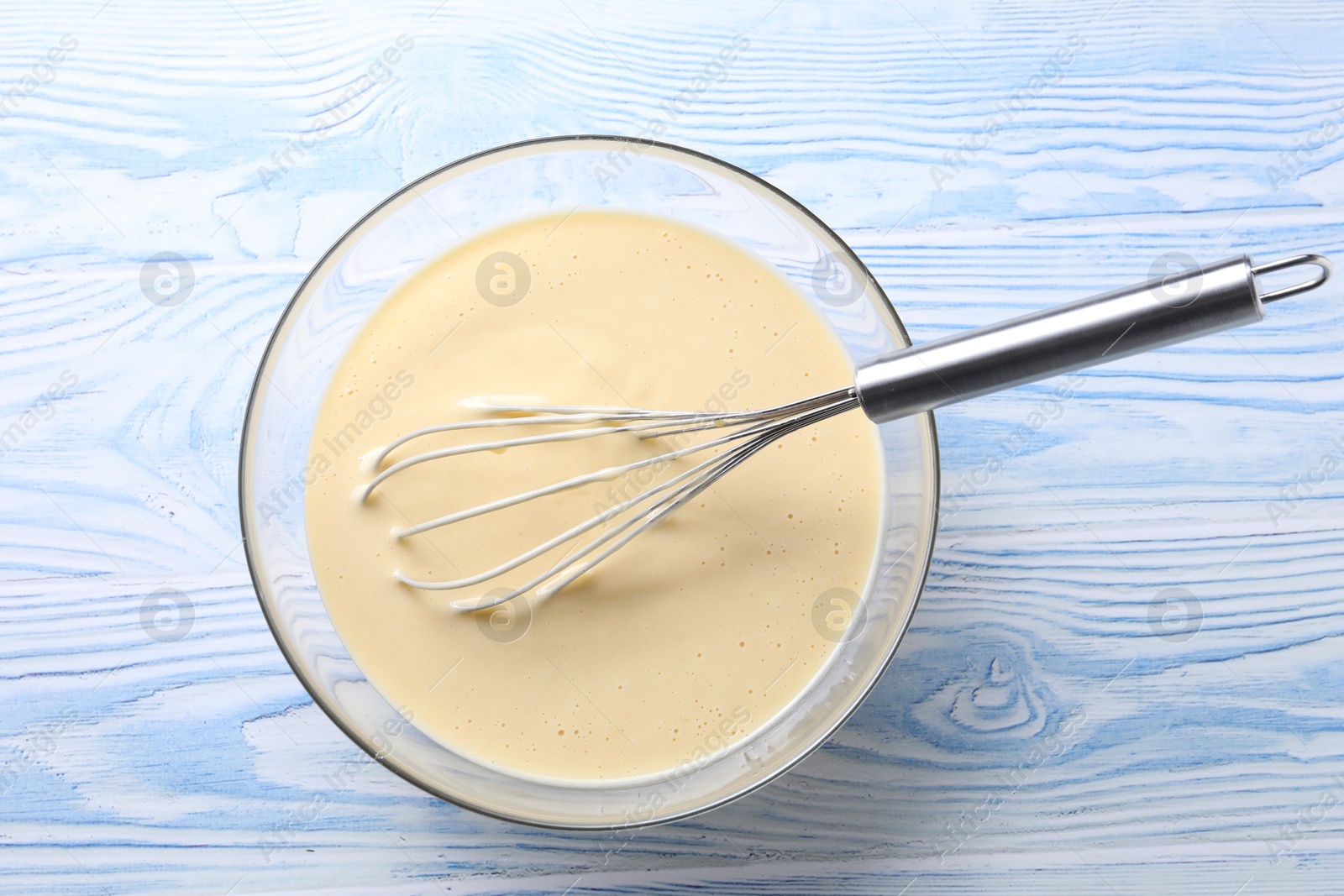 Photo of Whisk and bowl of dough on light blue wooden table, top view