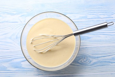 Photo of Whisk and bowl of dough on light blue wooden table, top view