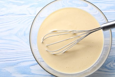 Photo of Whisk and bowl of dough on light blue wooden table, top view