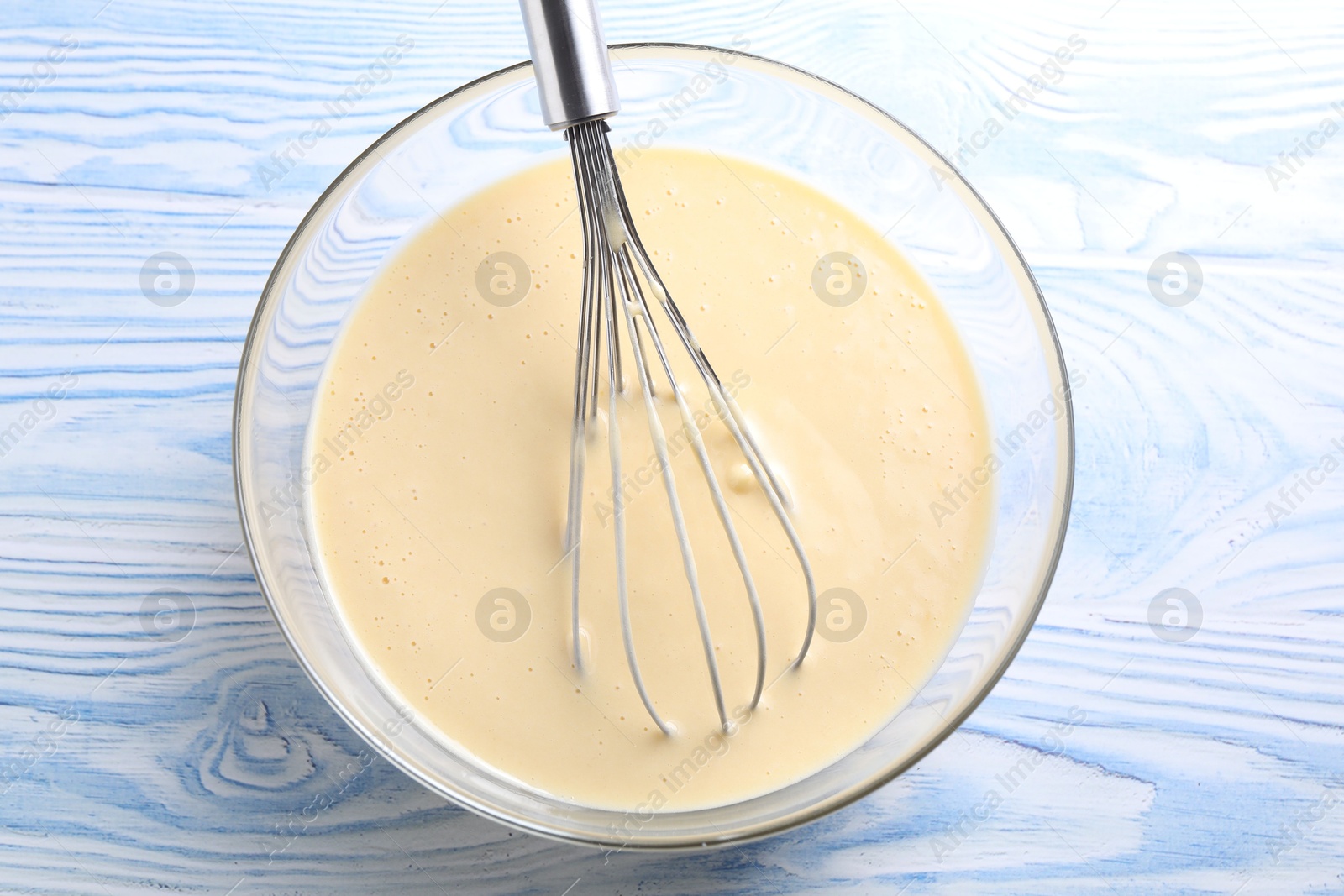 Photo of Whisk and bowl of dough on light blue wooden table, top view