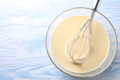 Photo of Whisk and bowl of dough on light blue wooden table, top view. Space for text