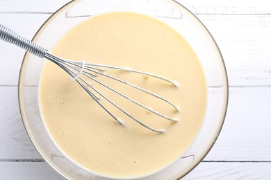 Photo of Whisk and bowl of dough on white wooden table, top view