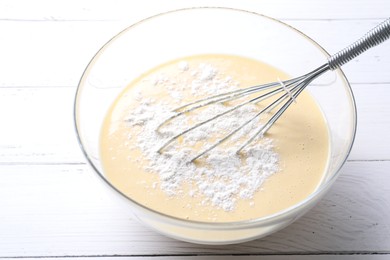 Photo of Whisk and bowl of dough on white wooden table, closeup